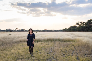 Naklejka na ściany i meble Young adult smiling Mexican woman standing in a dry grassy meadow looking at the camera