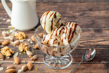 Almond, pistachio and walnut Roma ice cream in a glass bowl with caramel sauce poured over it.