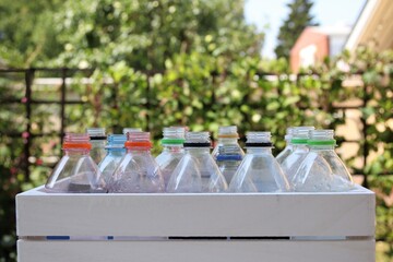 Empty plastic bottles in a wooden box waiting to be recycled. There were soft drinks and mineral water in the bottles. The box is outdoors in the garden.