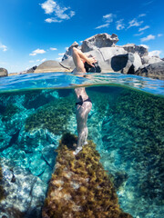 Young girl posing on the reef in a half underwater effect. Young lady enjoying the sun in the wonderful sardinian sea.