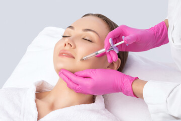 Cosmetologist makes rejuvenating anti wrinkle injections on the face of a beautiful woman. Female...