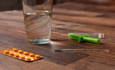 pastillas, termometro y vaso con agua sobre una mesa de madera