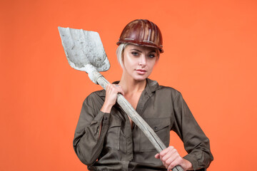 woman hard worker in protective helmet and boilersuit hold shovel on orange background, 1 may
