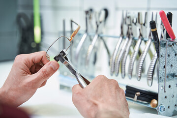 Male optician repairing glasses with pliers in workshop - obrazy, fototapety, plakaty