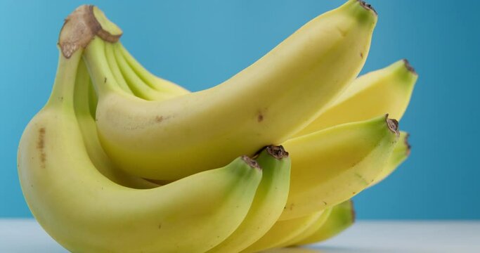 Yellow beautiful ripe bananas lying on the table on a blue background. Ripe bananas spin in a circle. Interesting angle, video footage.