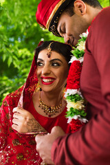 pleased indian man in turban hugging happy bride in red sari