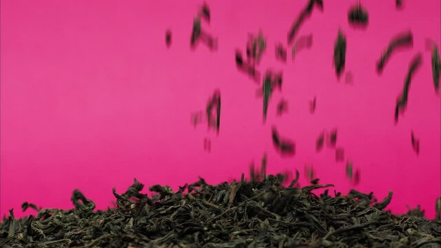 Close-up of falling down dried tea leaves on table on pink background. Shooting of black ceylon tea in studio. Macro footage of pouring out brewed tea into pile. Food and drink cooking video. 