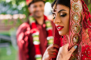 Indian bride in sari and headscarf near blurred man in turban on background