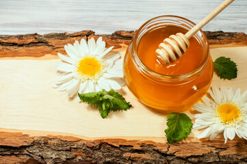 fresh honey in a jar on a wooden log with daisies. High quality photo