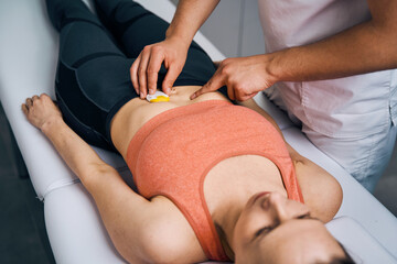 Therapist placing electrostimulator on woman stomach. Specialist in massage parlor puts electrodes