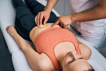 Wall murals Massage parlor Therapist placing electrostimulator on woman stomach. Specialist in massage parlor puts electrodes