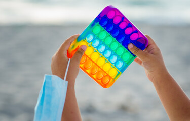 girl 5 years old in a swimsuit lying on a sun lounger by the sea on a sandy beach plays Pop It anti-stress on a hot sunny day.