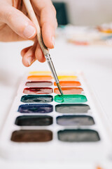 Close-up view of hand holding a brush and mixing the colors of paints on palette. Concept of art...