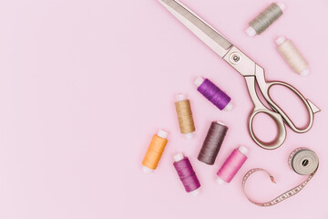 Tailor's work desk. Sewing accessories and fabric on a pink background. Sewing threads, needles, fabric, sewing centimeter or measuring tape. Top view. copyspace.