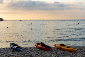 Kayaks on the seashore at sunrise, on a pebble beach at dawn.
