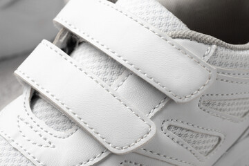 Photo of white children's sneakers. Macro photography of sports sneakers made of leather and fabric with Velcro fastener, top view, monochrome.