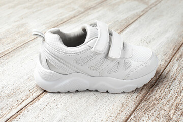 A white sneaker on a light background. One children's leather with fabric sports sneaker with Velcro fastener, photographed side view.