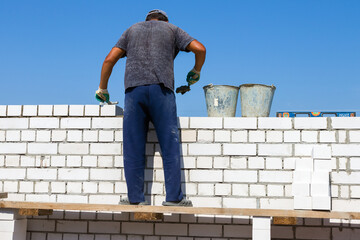 a bricklayer constructs a wall of a building from white sand-lime bricks