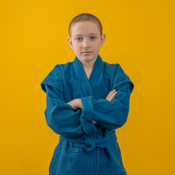 a boy in a blue kimono for sambo folded his arms over his chest on a yellow background