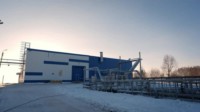 Workshop building near metal bridge over processing reservoirs at wastewater treatment station at sunset light in winter