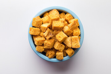 Square-shaped bread crumbs in a blue pot on a white background. Oven-fried golden brown bread crumbs. Close-up.