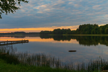 Fototapeta na wymiar View of the lake at sunset. Above the lake thick clouds, a wooden footbridge enters the water