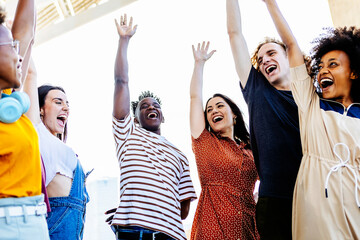 Group of young friends raising their hands in unity - Happy multiracial people having fun together and celebrating victory outdoors - Low angle view - Unity, integration and community concept - Focus - Powered by Adobe