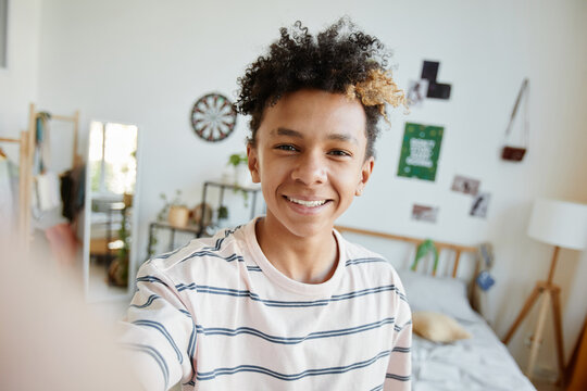 POV of mixed-race teenage boy smiling at camera during video chat or live stream in cozy room, copy space