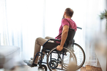  Man in Wheelchair looking out of a window at home. Rear view of mature man in wheelchair look thru...