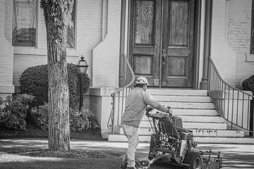 professional landscaper man standing on mower and mowing lawn or grass in front of church