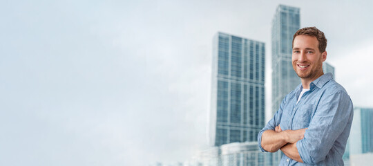 Smiling business man portrait in city background. Confident young caucasian male businessman happy with arms crossed at condo building towers as realtor or homeowner. Career success lifestyle.