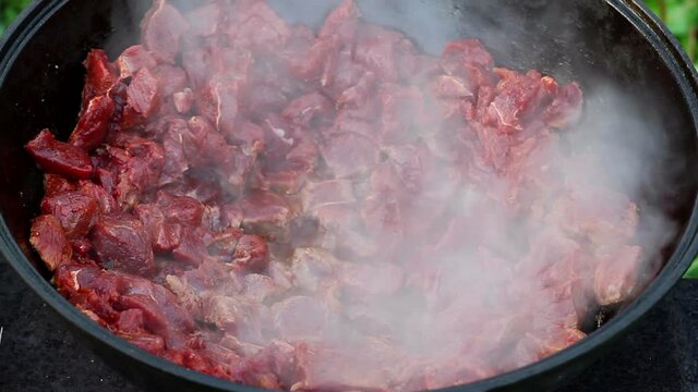 red meat gurgles and boils in oil in a large cauldron. cooking process of an oriental dish. traditional asian dish