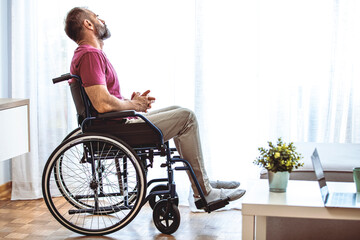 Side view of mature man sitting in wheelchair and looking away. Side view of thoughtful disabled active Caucasian man looking through window on wheelchair in a comfortable home