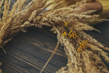 Stylish autumn boho wreath with dry grass and wildflowers on rustic wooden background. Making rustic autumn wreath with pampas grass and yellow tansy flowers, holiday workshop