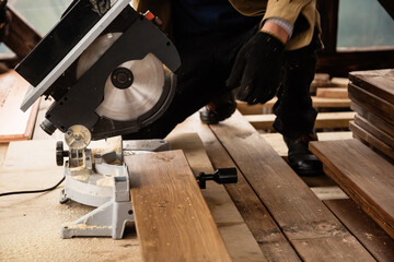 Miter saw with a large metal blade in the hands of a carpenter. Working tool for sawing wooden planks. A close-up of the sawing process. Labor protection and safety rules for the use of power tools