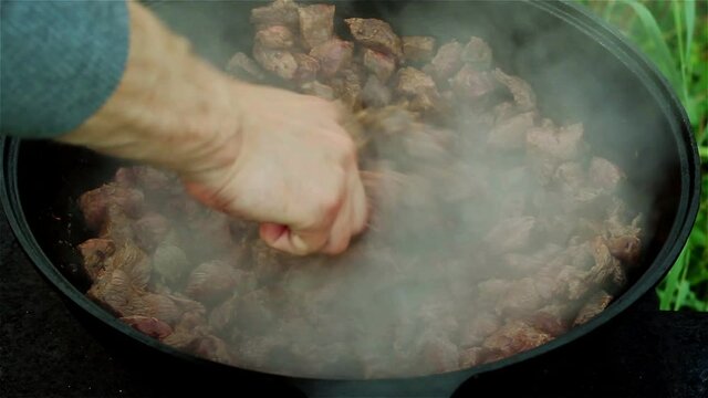 meat stew in a pot. white man's hand with wooden spoon mixes the dish