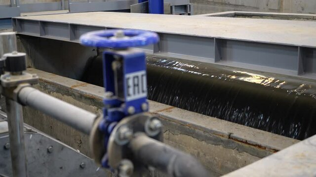 Pipe with blue valve and flange against water pouring into reservoir in purification station workshop close view
