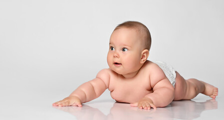 Six month old baby girl in a diaper lying and looking with interest to the side on a white background