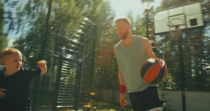Basketball players sportive family father and son dribbling on basketball court outdoors. Active energetic workout