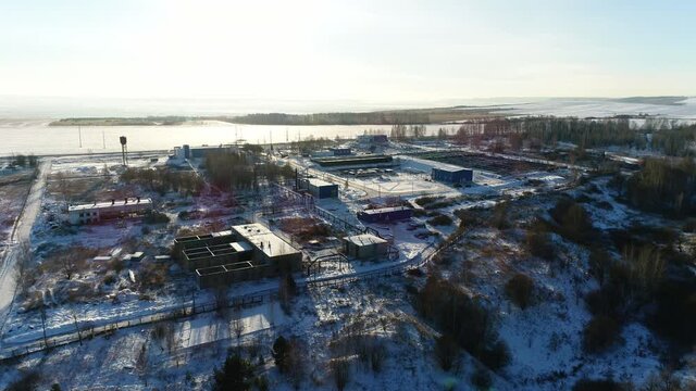 Wastewater treatment plant with pools and workshops on snowy hill against frozen river at sunset in winter bird eye view