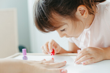 Obraz na płótnie Canvas Six year preschooler girl with interest paint nails her moms with nail polish