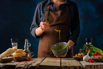 There are many ingredients on the wooden table for making the classic Caesar salad. The cook prepares mustard sauce for the salad. Delicious restaurant dish.