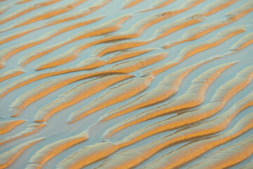Sand waves texture with water on the sea beach. Yellow sand texture for background.