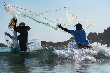 Fisherman in action throwing fishing nets into the sea with strong waves on the seashore