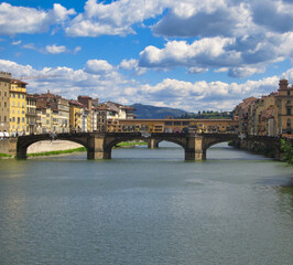 Fototapeta premium Medieval Ponte Vecchio bridge over the Arno river under a blue cloudy sky in Florence