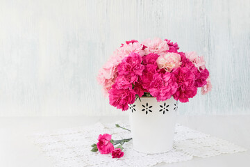 Pink carnation flowers bouquet in white vase on blue background.