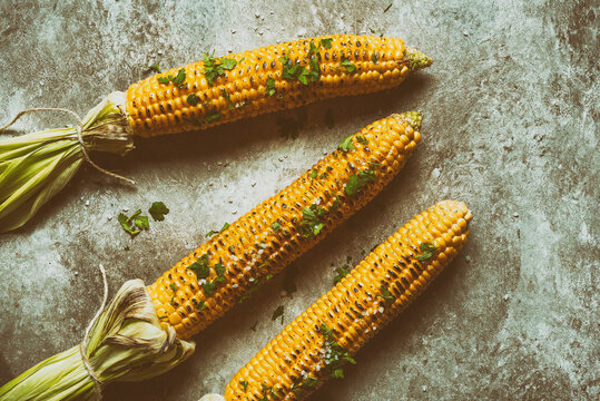 Grilled sweet corn on a dark grunge background. Toned image. Top view, flat lay. Rustic style. Summer vegan dinner.