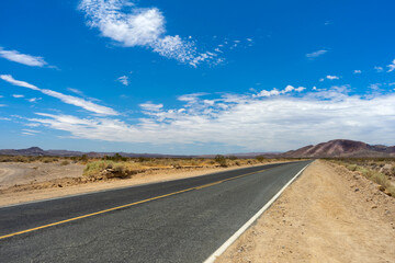 Obraz na płótnie Canvas Long Mojave Desert road with cloudy blue sky