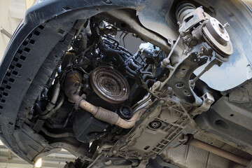 Modern car in a car service on a lift. on the car, the gearbox was removed for repair. The flywheel, elements of the exhaust system are visible. Selected focus.