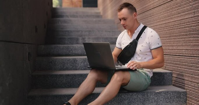 Man freelancer opening and using laptop PC sitting on the city stairs